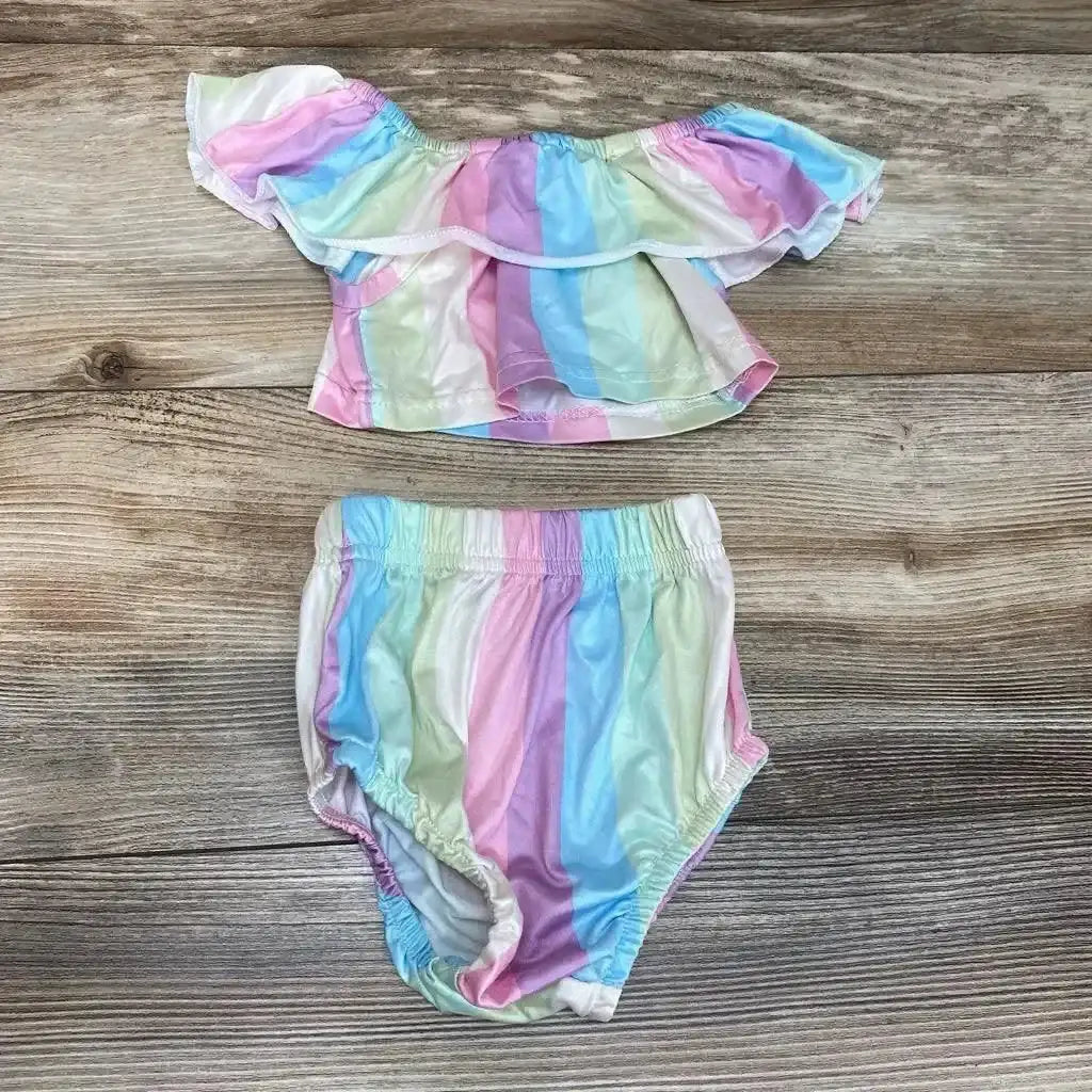 Flat lay of Rorychen 2-piece off-shoulder top and elastic-waist bottoms in pastel rainbow stripes on wood background, size 3-6m