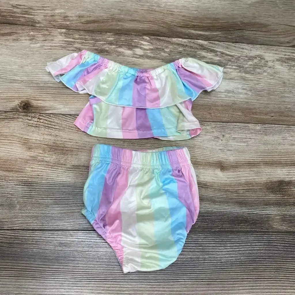 Flat lay of baby two-piece striped set with pastel rainbow off-shoulder ruffle top and elastic-waist bottoms on wood background