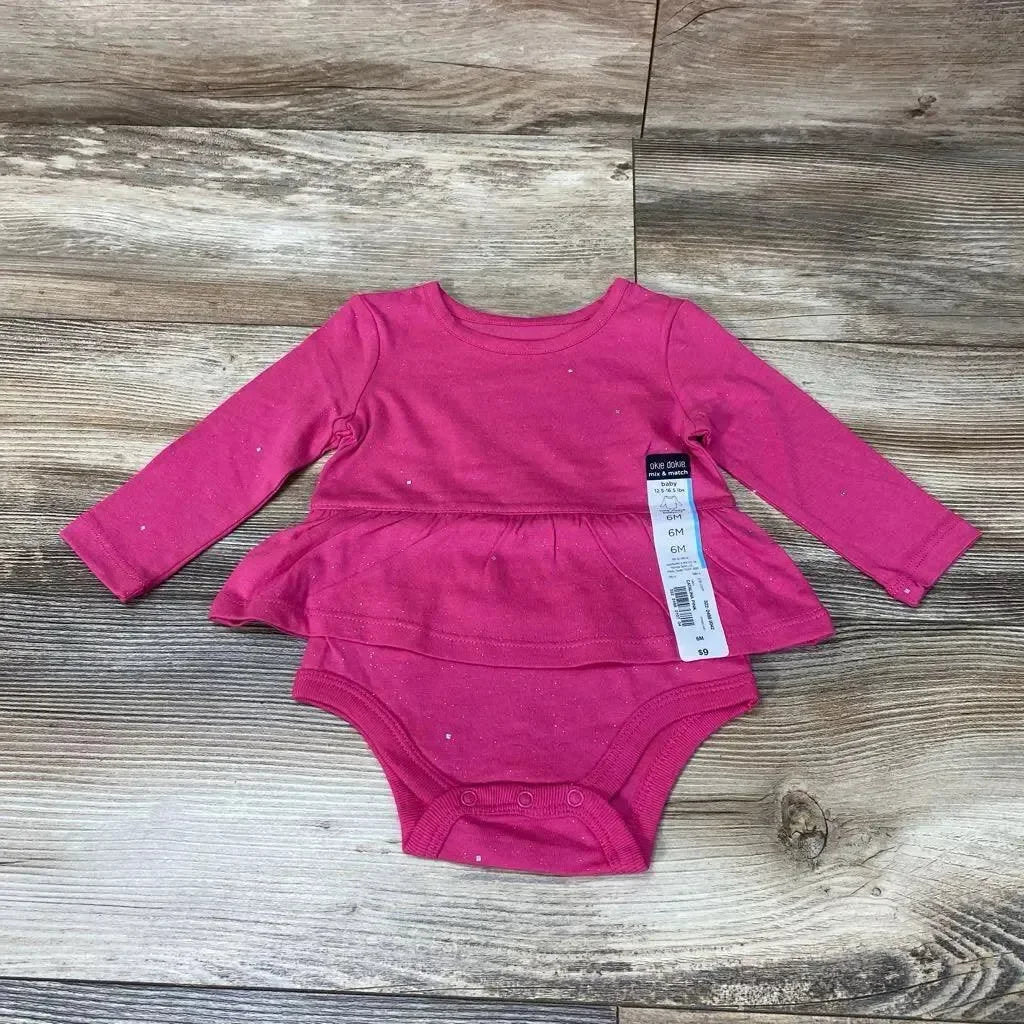 Flat lay of pink long-sleeve skirted bodysuit size 6M showcasing peplum skirt and snap crotch closures on wood floor background