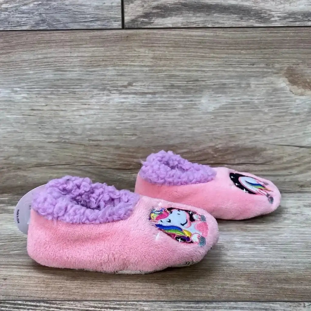 Side view of pink toddler slippers (size 5/6) showcasing unicorn patch on toes and purple fleece lining with wood floor background