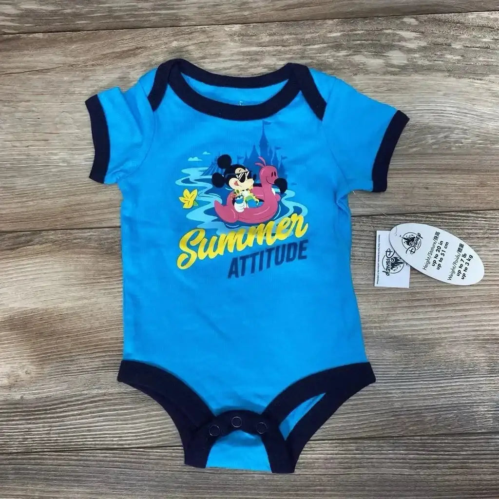 Flat lay of blue newborn Disney bodysuit with Mickey on a pink float and Summer Attitude text on wood background