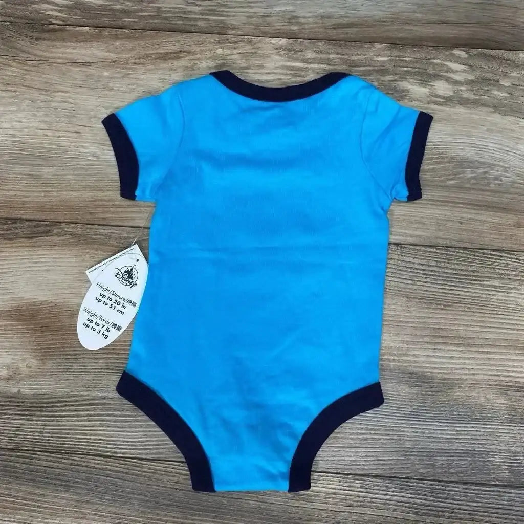 Back view of newborn bright blue Disney bodysuit with navy trim and attached tag on wood background