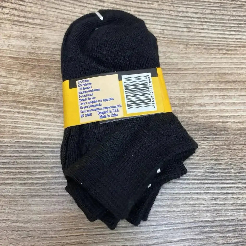 Top-down view of three-pack black baby socks (size 0–12) folded with yellow label and barcode on wood background