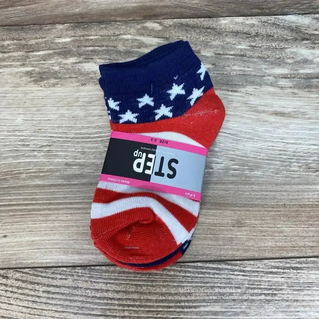Top-down view of toddler ankle socks (size 2–3) showcasing navy cuff with white stars and red-and-white stripes, wrapped with a gray 'STEP up' label on wooden background