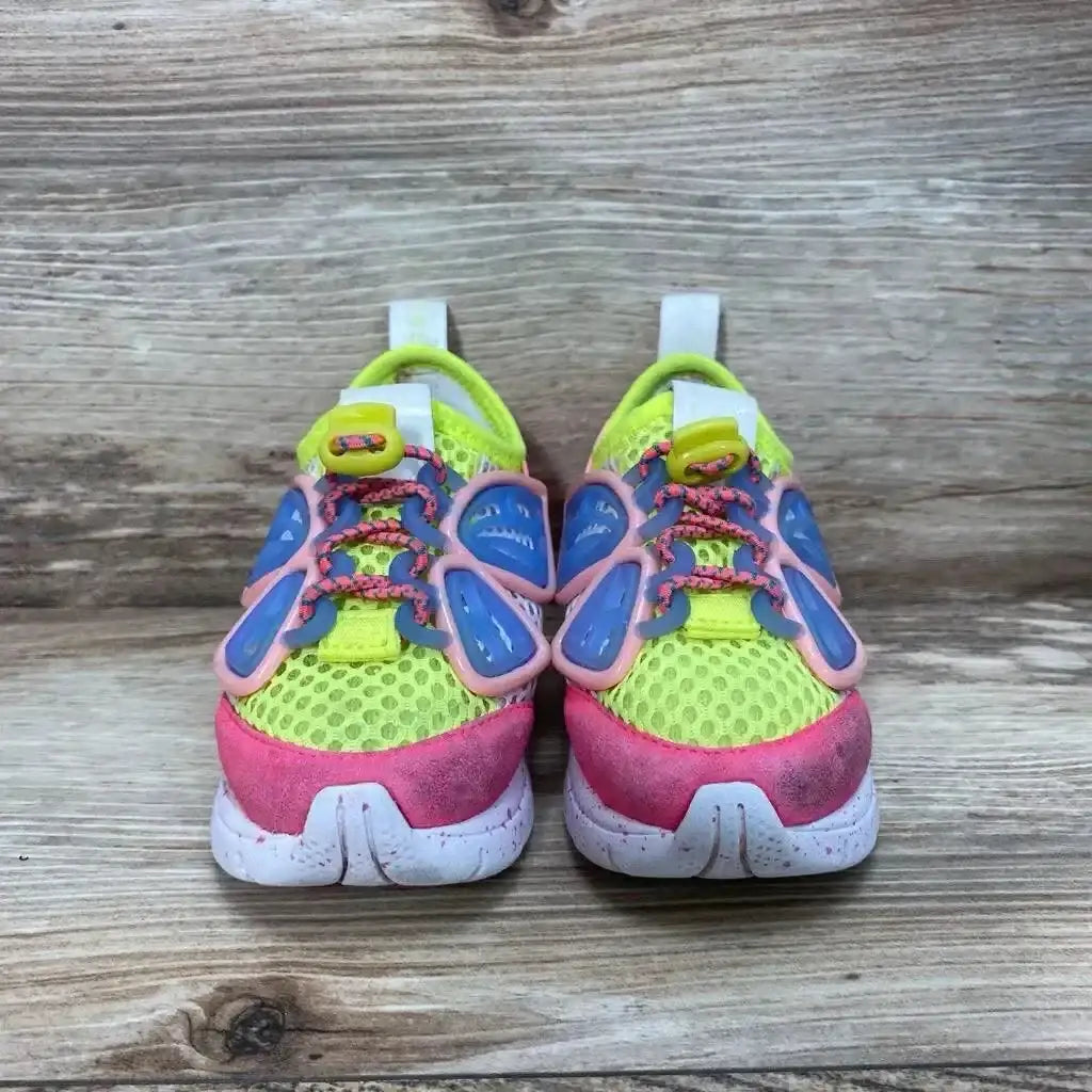 Front view of Sophia Webster Mini Chiara toddler sneakers showcasing neon yellow mesh, pink toe caps and blue-and-pink butterfly overlays on wood background