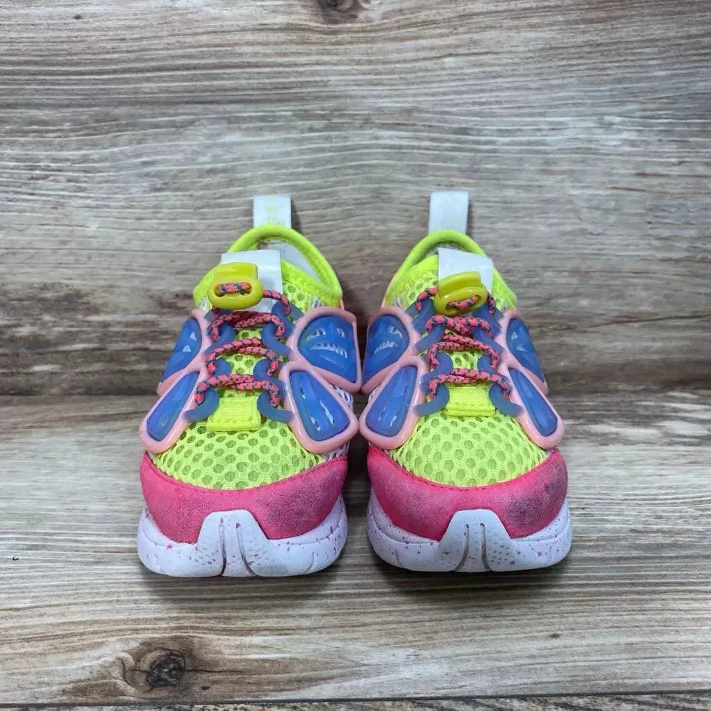 Front view of Sophia Webster Mini Chiara toddler sneakers showcasing neon yellow mesh, pink toe caps and blue-and-pink butterfly overlays on wood background