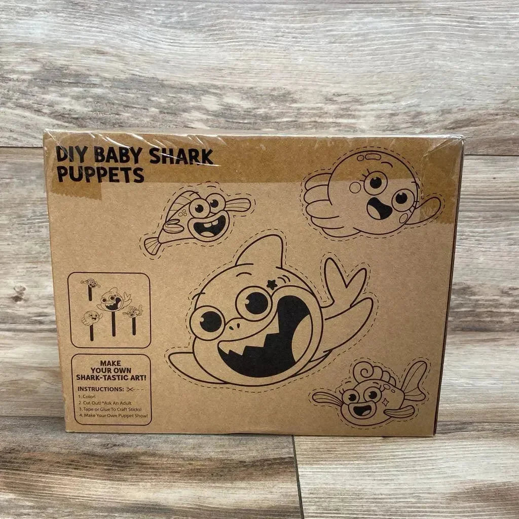 Front view of boxed DIY Baby Shark puppets showing printed cut-out characters and instructions on wood floor