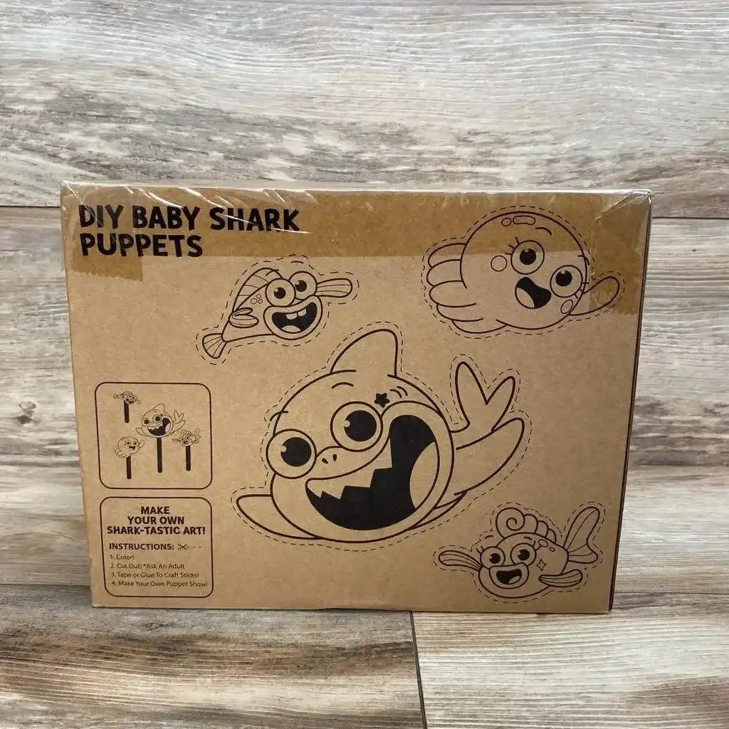 Front view of boxed DIY Baby Shark puppets showing printed cut-out characters and instructions on wood floor