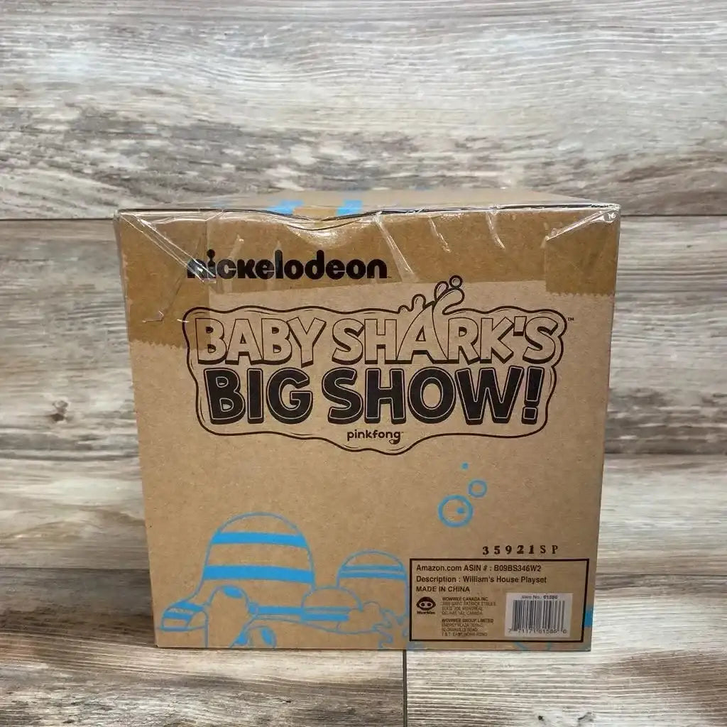 Front view of Baby Shark's Big Show William's House playset box showing logo and blue artwork on cardboard with wood backdrop