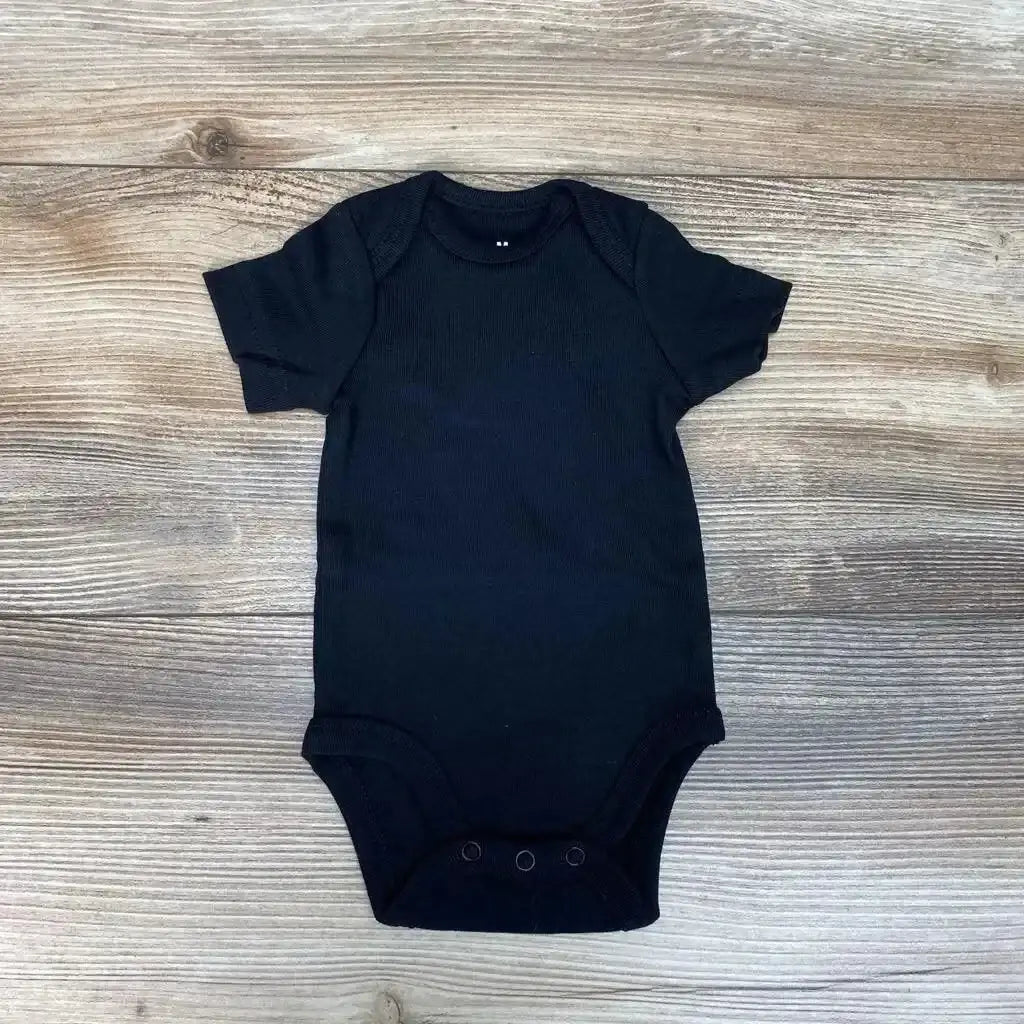 Flat lay of black newborn organic short-sleeve bodysuit with envelope shoulders and three snap crotch on wood background