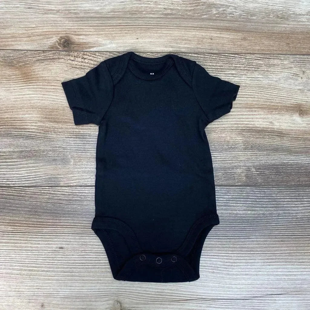 Flat lay of black newborn organic short-sleeve bodysuit with envelope shoulders and three snap crotch on wood background