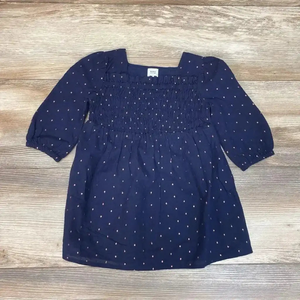 Flat lay of navy Baby Gap smocked dot dress showcasing smocked bodice, long sleeves, and small pink dots on a wood background
