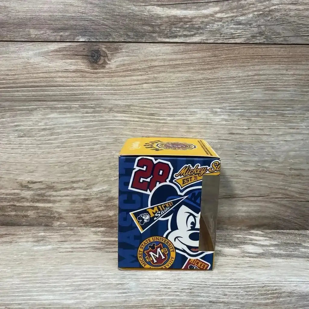 Front view of NEW Disney Vinylmation Mascot Series Goofy figure in sealed Mickey State University collegiate themed box on wood plank floor