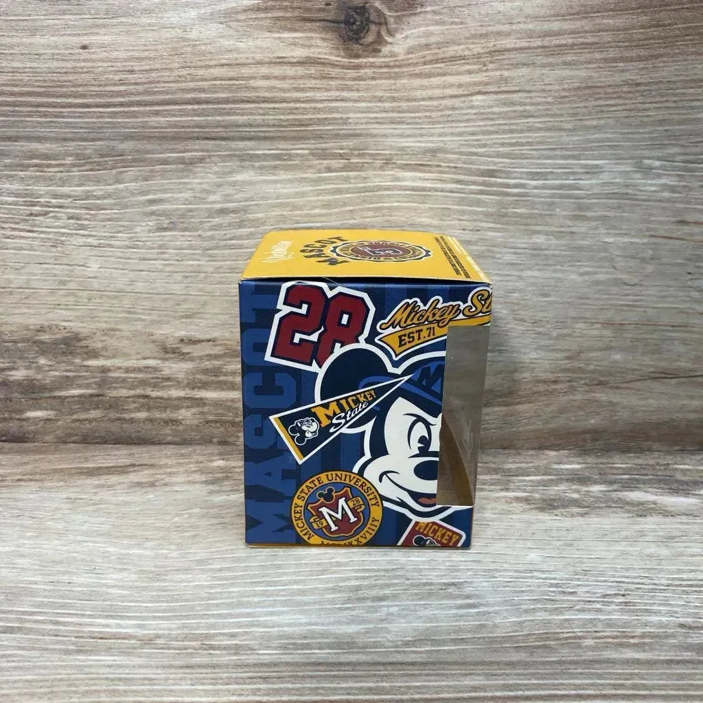 Front view of boxed Disney Vinylmation Pluto 3-inch figure showcasing Mascot Series blue and yellow packaging with Mickey graphics on wood backdrop