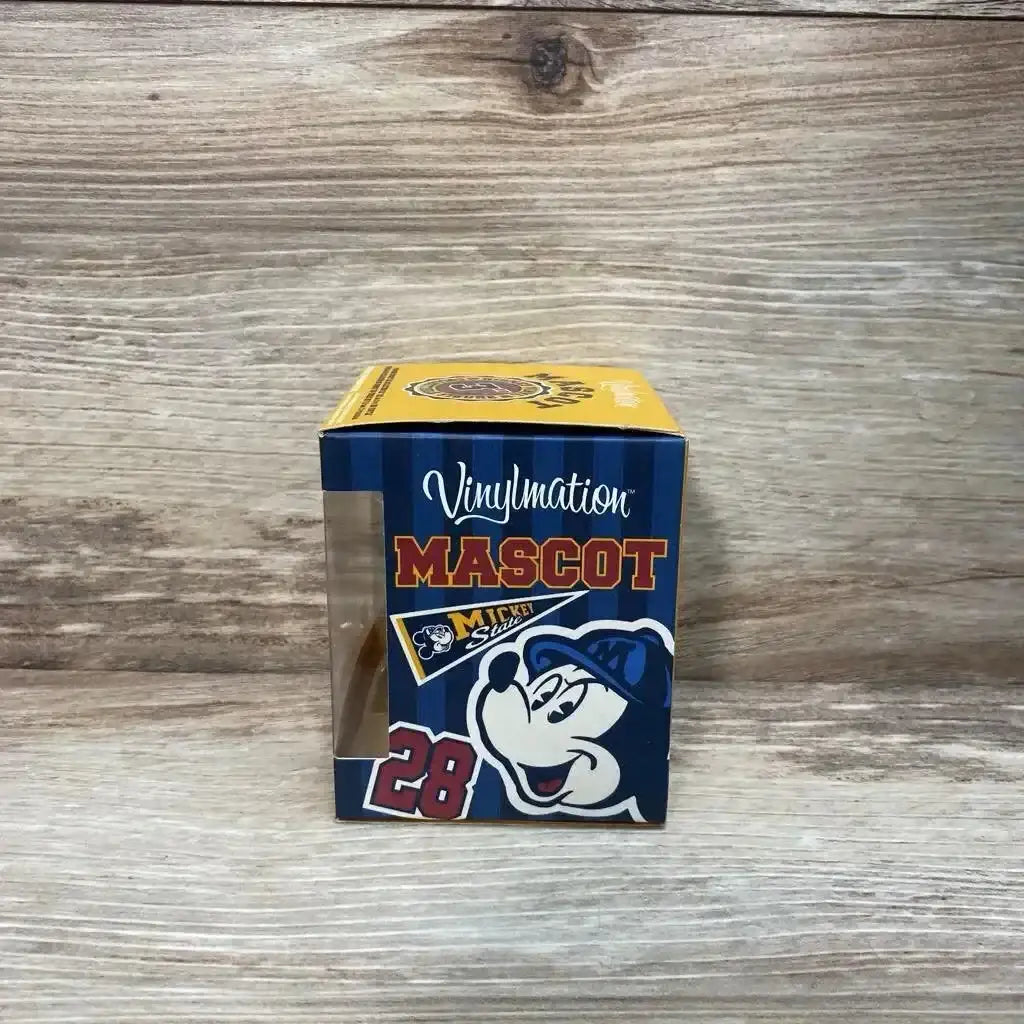 Front view of 3-inch Disney Vinylmation Mascot Pluto in box showing clear window and blue striped packaging on wood backdrop