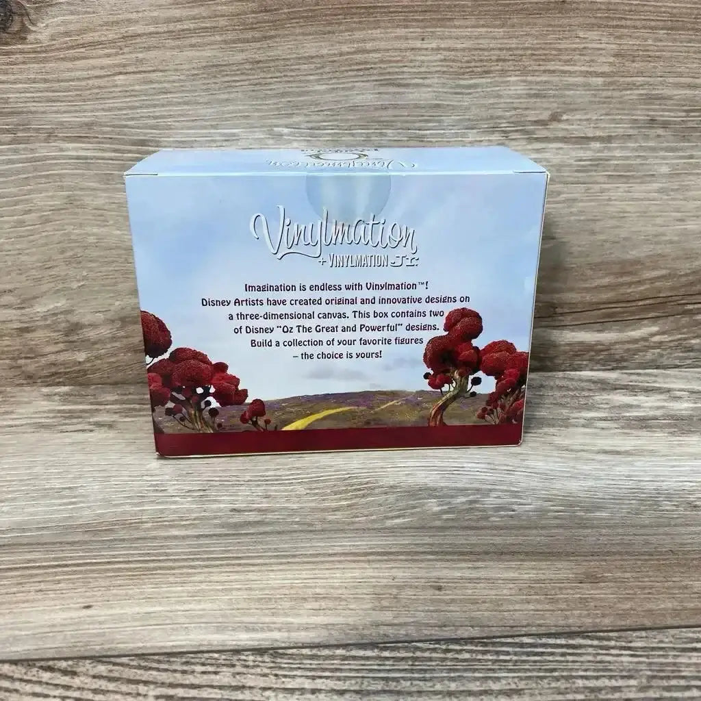 Front view of Vinylmation 'Oz The Great and Powerful' box showing logo, description text, and red tree illustration on light wood background