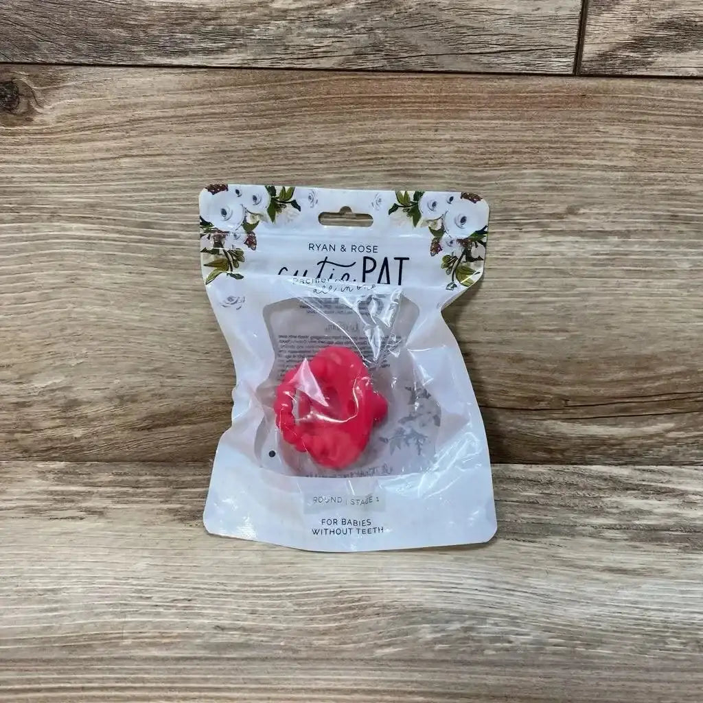 Front view of Ryan & Rose Cutie PAT round pacifier and teether in pink inside clear retail pouch on wood background