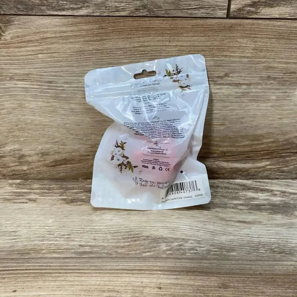 Rear view of Ryan and Rose Cutie PAT round pacifier and teether (pink, 0-6m) inside resealable floral pouch on wooden surface