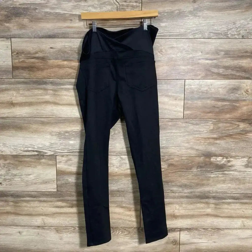 Back view of Isabel maternity crossover pants in black showing crossover belly panel and back pockets on wood floor