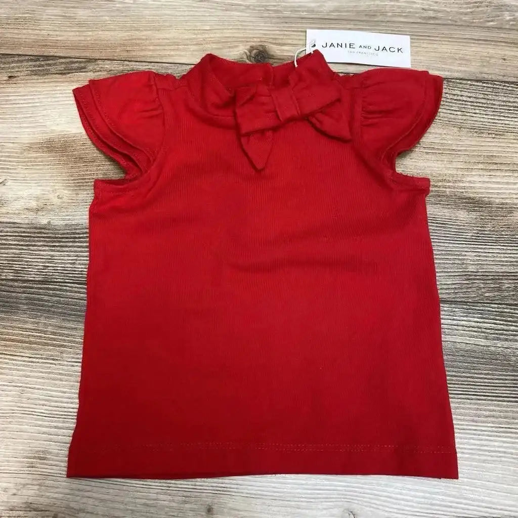 Flat-lay front of red Janie & Jack baby top showing ruffle sleeves and bow neckline on light wood background