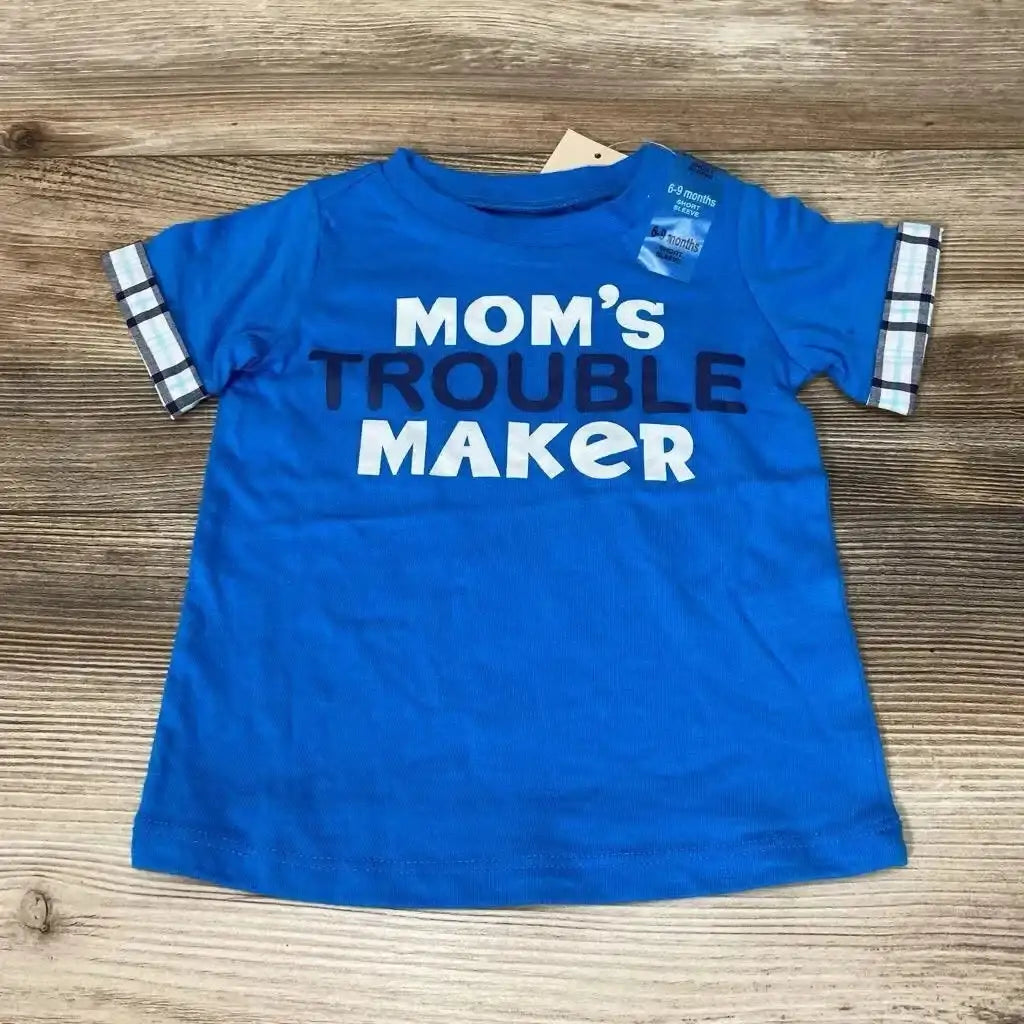 Flat lay of blue Mom's Trouble Maker baby T-shirt showcasing plaid sleeve cuffs and visible 6-9 months tag on wood background