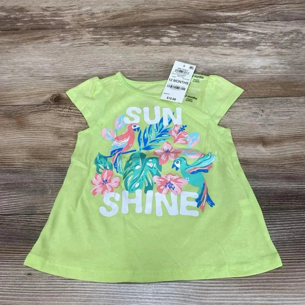 Flat lay of lime green toddler T-shirt showing white SUN SHINE text and colorful tropical birds and flowers on wood table