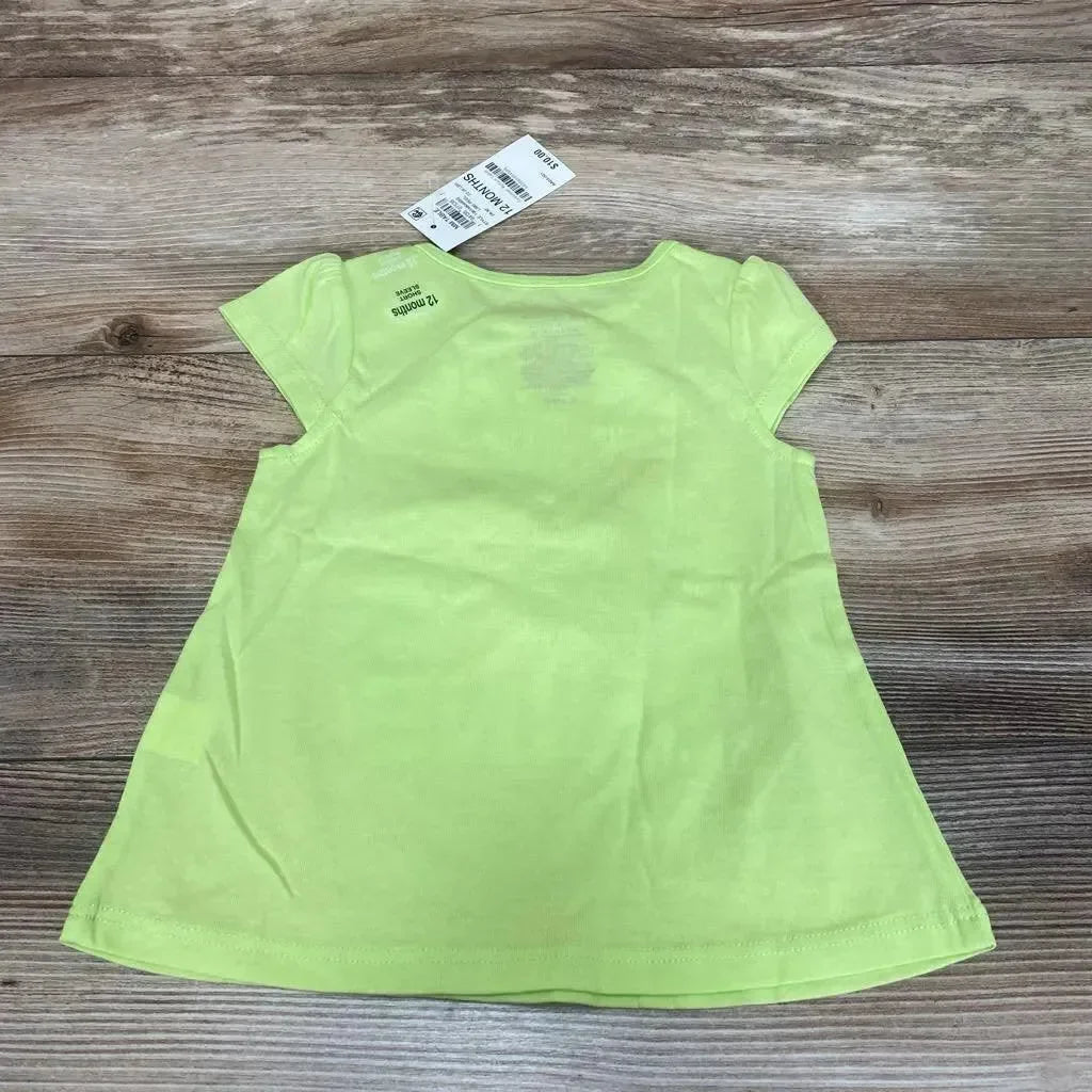 Back view of green baby t-shirt, 12 months, laid flat showing A-line hem, short puff sleeves, retail tag on wood background