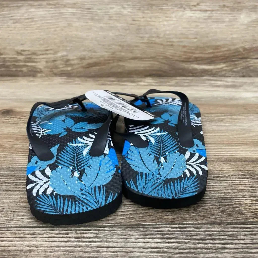 Front view of toddler size 13c Juncture blue flip-flop sandals with tropical leaf print and black straps on wood background