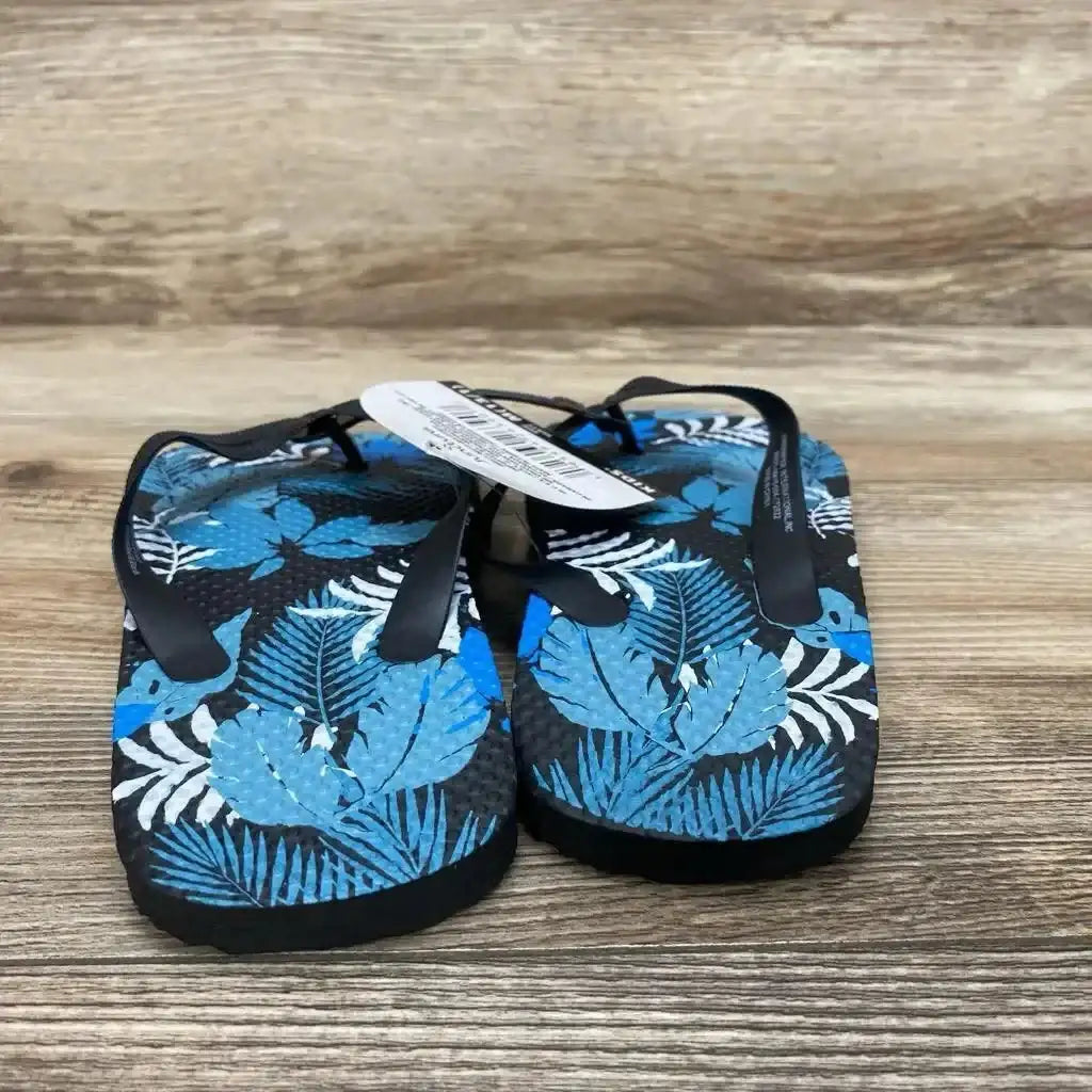 Front view of toddler size 13c Juncture blue flip-flop sandals with tropical leaf print and black straps on wood background