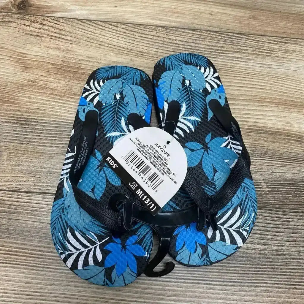 Top view of NEW Juncture Blue Jungle Sandals sz 13c flip-flop showcasing tropical leaf print with black straps and retail tag on wood background