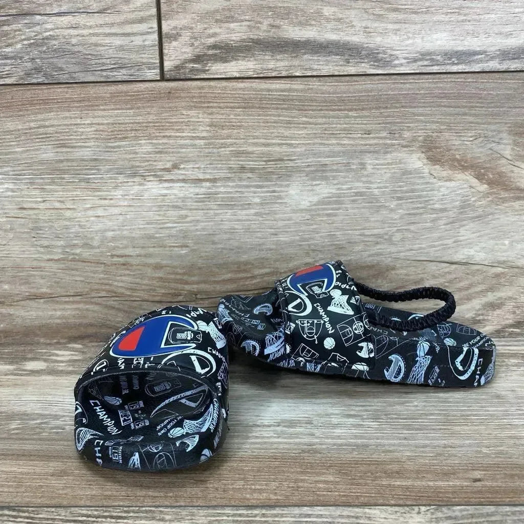 Angled view of black Champion Super Slide sandal size 8C with doodle print, logo patch and elastic heel strap on wood floor