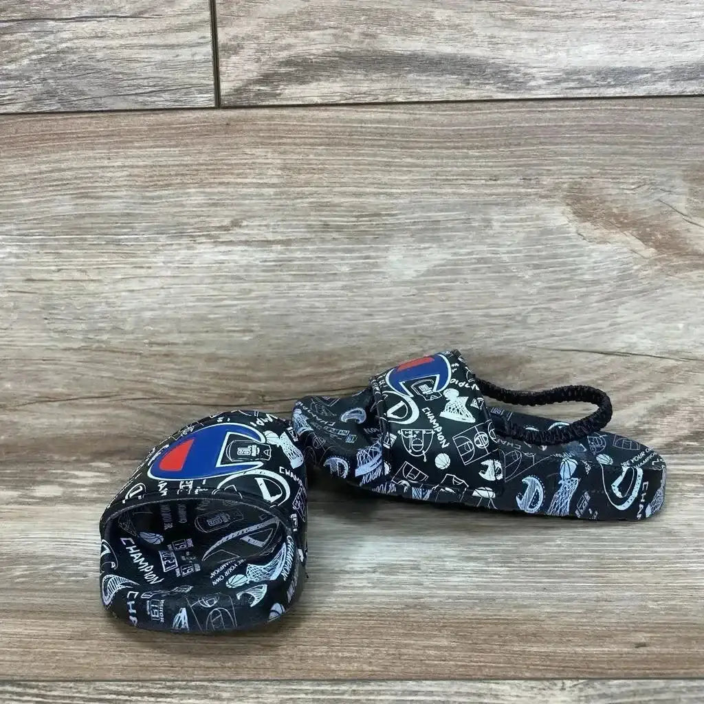 Angled view of black Champion Super Slide sandal size 8C with doodle print, logo patch and elastic heel strap on wood floor