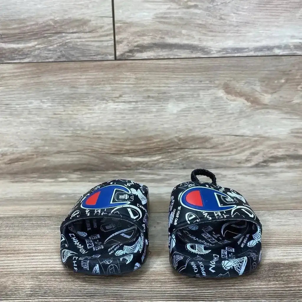 Angled view of black Champion Super Slide toddler sandal, size 8C, showing doodle-printed strap and textured footbed on white background