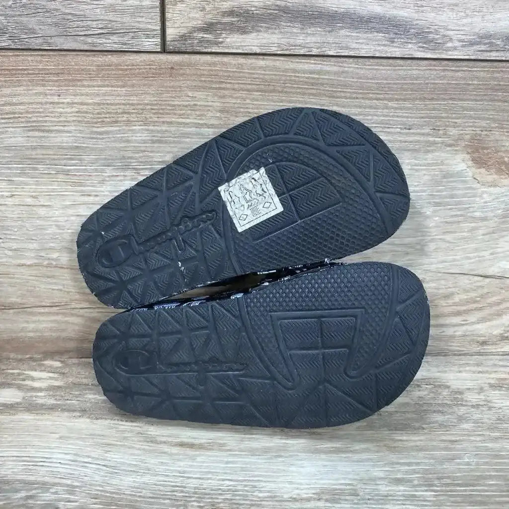 Bottom view of Champion Super Slide Doodle sandals sz 8c showcasing black rubber tread with embossed Champion logo on wood plank floor
