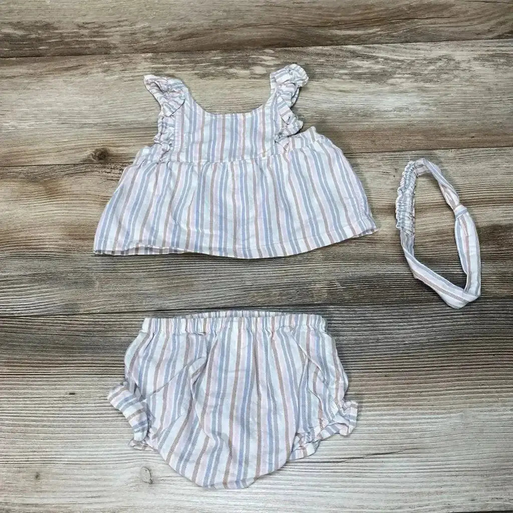 Flat lay of baby three-piece striped top, bloomers, and matching headband showing pastel vertical stripes and ruffle shoulder straps on wood floor
