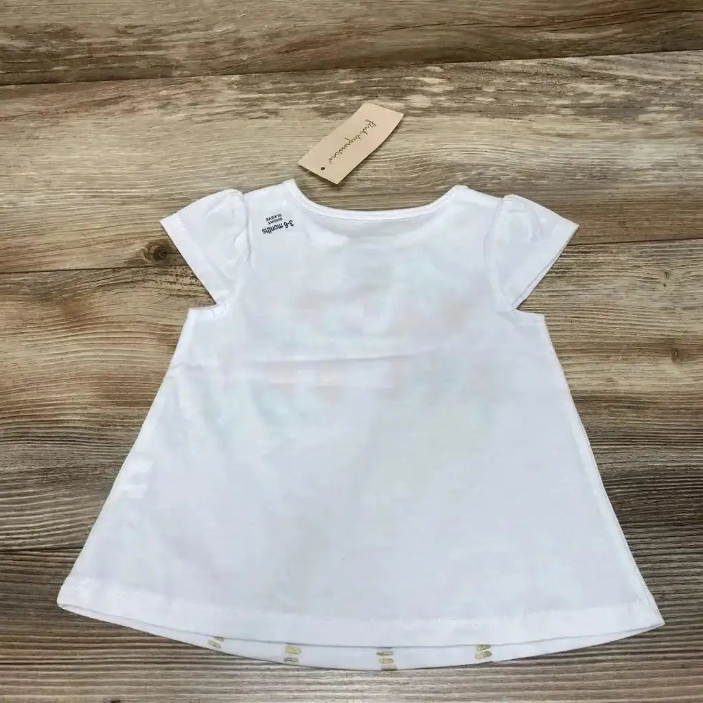 Back view of white baby shirt size 3 to 6 months showcasing cap sleeves and A-line flared hem on wood plank background