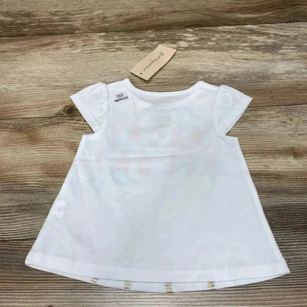Back view of white baby shirt size 3 to 6 months showcasing cap sleeves and A-line flared hem on wood plank background