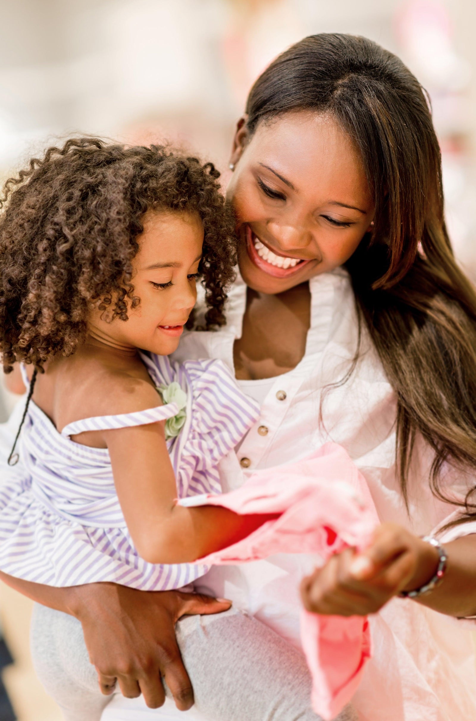Mother holding her young daughter while they examine a pink kids' shirt in a bright clothing store