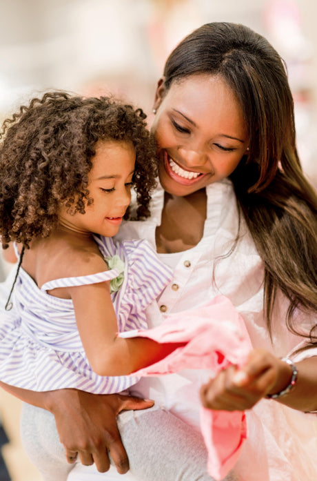 Mother holding her young daughter while they examine a pink kids' shirt in a bright clothing store