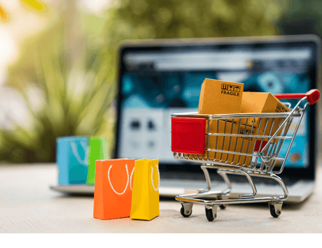 Mini shopping cart with cardboard boxes and colorful small shopping bags in front of a laptop, representing online shopping