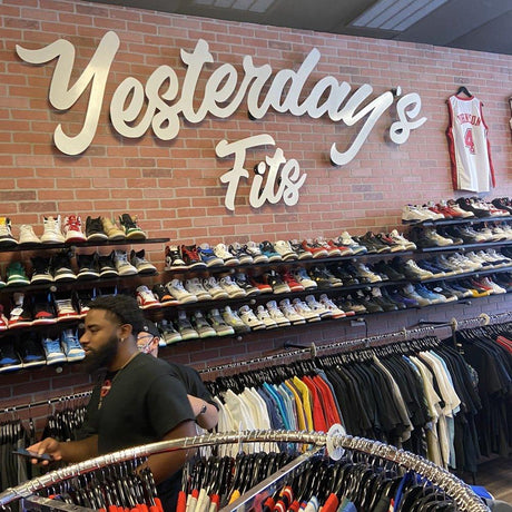 Customers browsing racks of kids clothing and rows of sneakers in a resale store beneath a brick wall sign reading Yesterday's Fits