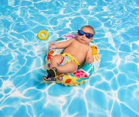 Baby wearing sunglasses lounging in a colorful inflatable ring on a bright swimming pool