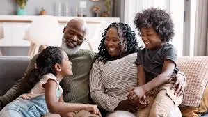 Grandparents sitting on a couch laughing and hugging two young grandchildren in a cozy living room