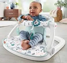 Front view of Sit Me Up floor seat with padded patterned base, toy arch, and tray showing a baby seated on a living room floor