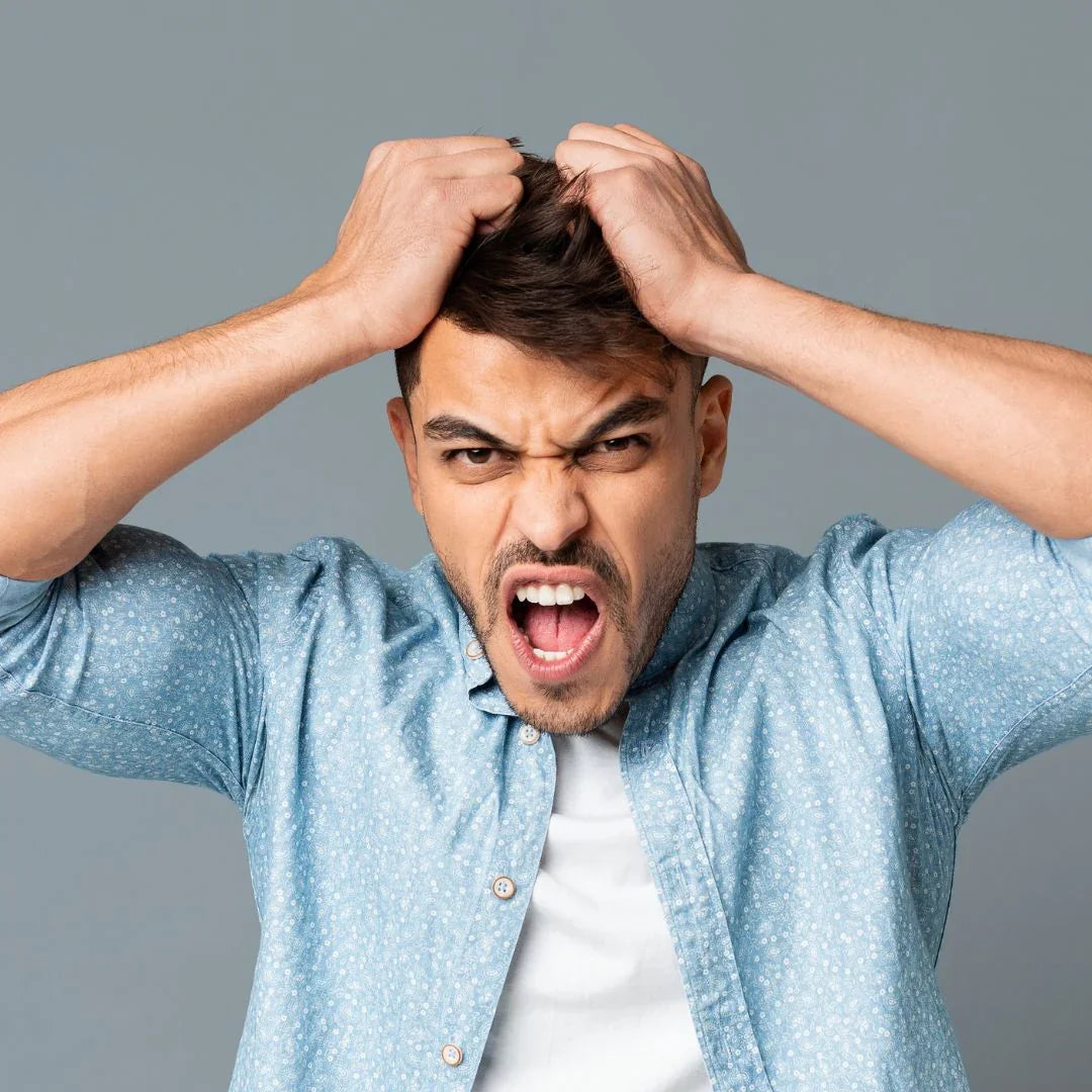 Frustrated man in blue shirt pulling his hair with an angry expression against gray background