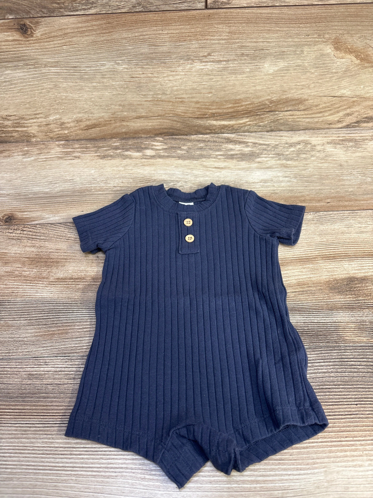 Flat lay of navy ribbed Henley shortie romper (3M) showing two wooden buttons and short sleeves on wood background