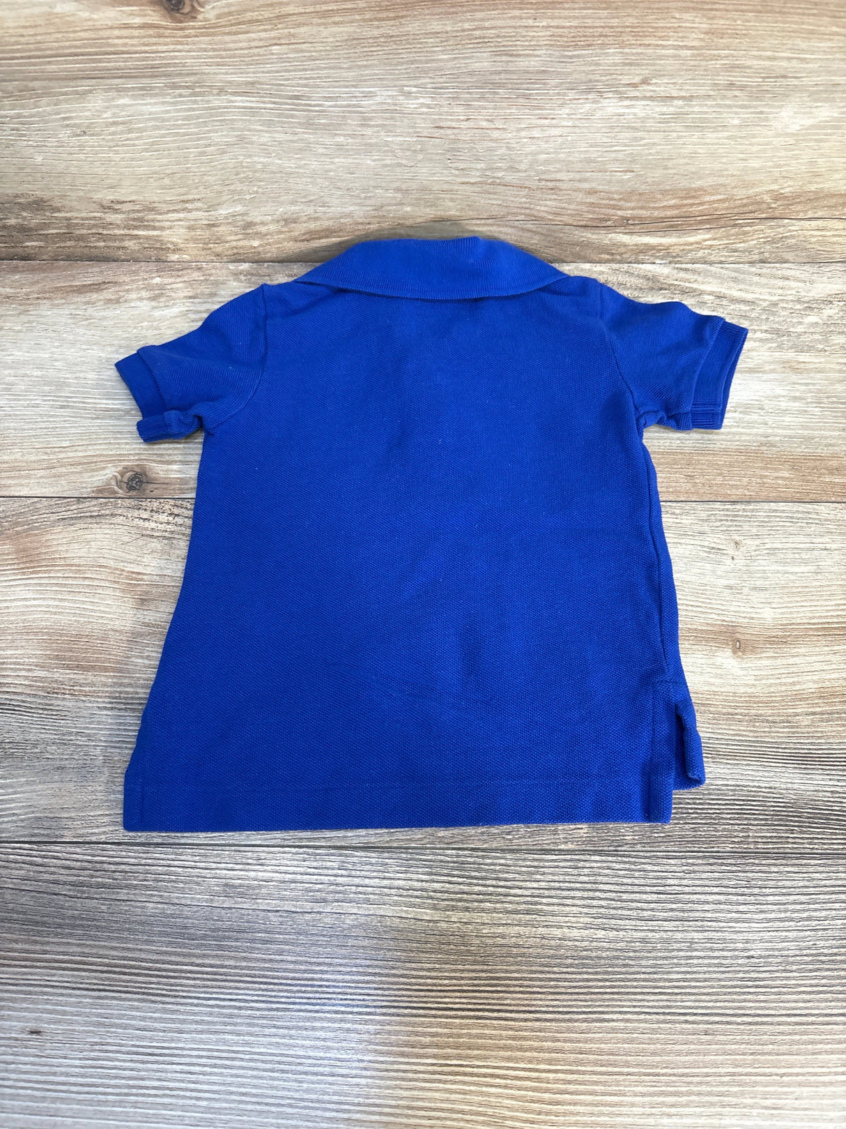 Back view of a blue short sleeve kids polo shirt on wood background