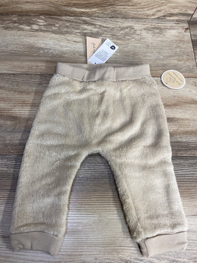 Beige soft fuzzy baby pants with elastic waistband and cuffs on wooden background