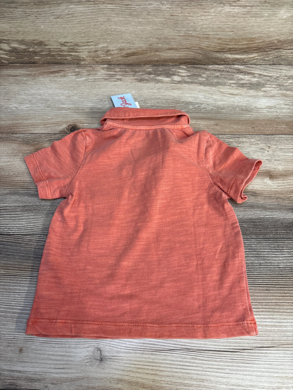 Coral baby onesie with short sleeves and ribbed texture, laid flat on wood surface