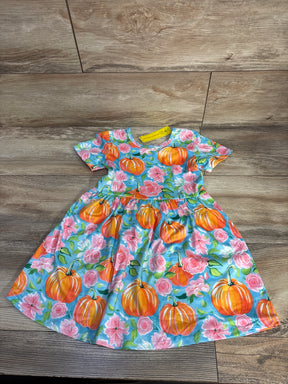 Toddler dress with orange pumpkin and pink flower print on blue fabric laid on wooden floor